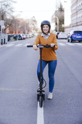 Smiling woman standing with electric push scooter on road - EBBF08489