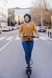 Glückliche Frau mit Elektro-Scooter auf der Straße stehend - EBBF08491