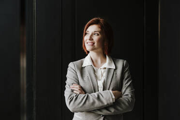 Happy businesswoman standing with arms crossed in office - EBBF08504