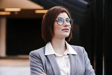 Smiling businesswoman wearing eyeglasses in office - EBBF08507