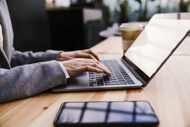 Businesswoman typing on laptop in office cafeteria - EBBF08510