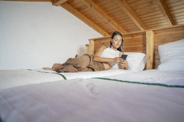 Junge Frau liegt auf dem Bett und benutzt ein Smartphone zu Hause - FBAF02127