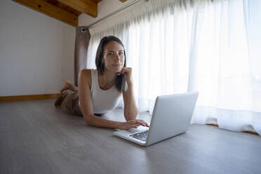 Freelancer lying on floor near laptop at home office - FBAF02132