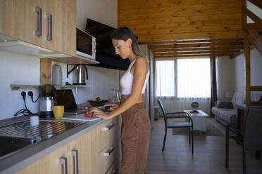 Young woman cutting tomato in kitchen at home - FBAF02134