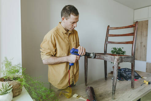 Mann restauriert alten Holzstuhl mit Elektrowerkzeug auf Tisch zu Hause - YTF01766
