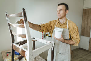 Man holding paint can and coloring chair at home - YTF01779