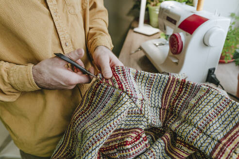 Man cutting patterned cloth with scissors at home - YTF01783