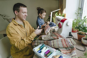 Man cutting fabric with daughter using scissors at home - YTF01785