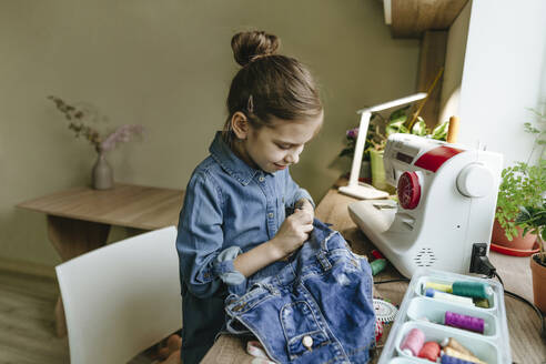 Smiling girl cutting old clothes by sewing machine at home - YTF01787