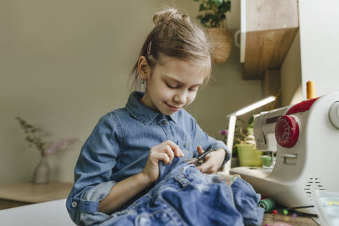 Smiling girl cutting cloth with scissors at home - YTF01788