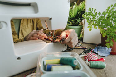 Man sewing recycled clothes through machine at home - YTF01793