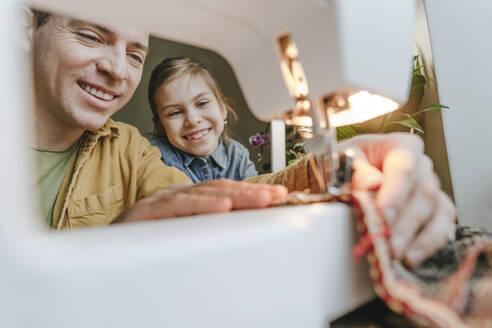 Smiling daughter and father sewing recycled clothes through machine - YTF01795