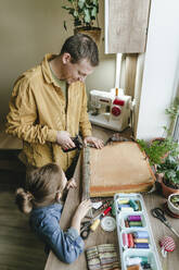 Tochter und Vater befestigen Stoff von alten Kleidern auf einem Stuhl mit einem Hefter zu Hause - YTF01802