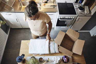 Hochformatige Ansicht einer Frau mit Behinderung, die in der Küche zu Hause ein Paket öffnet - MASF42215