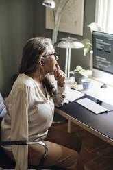 Side view of mature female freelancer with disability sitting at desk in home office - MASF42220