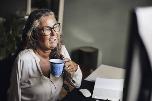 Reife Geschäftsfrau hält Tasse während eines Videoanrufs im Heimbüro - MASF42222