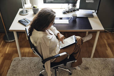 High angle view of businesswoman using tablet PC while sitting on chair at home office - MASF42229