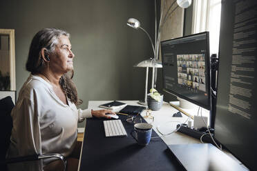 Businesswoman doing video conference through computer while sitting at desk in home office - MASF42232