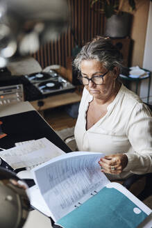 High angle view of businesswoman examining reports while sitting at desk in home office - MASF42236