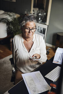 Geschäftsfrau mit Behinderung fotografiert Dokumente, während sie am Schreibtisch im Home Office sitzt - MASF42238
