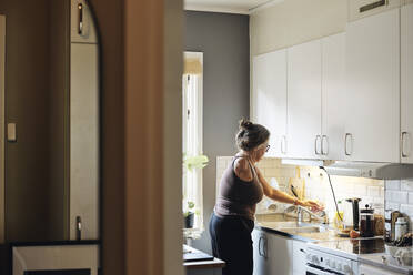 Seitenansicht einer Frau mit Behinderung, die bei der Arbeit in der Küche zu Hause den Wasserhahn zudreht - MASF42244