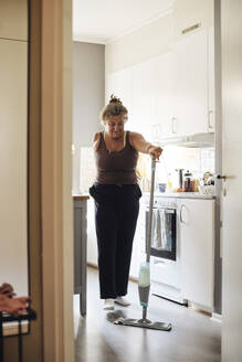 Ältere Frau mit Behinderung wischt den Küchenboden zu Hause - MASF42246
