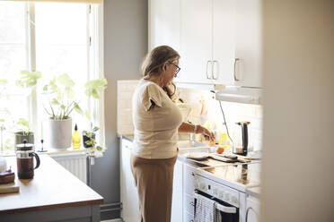 Side view of mature woman with disability preparing breakfast while standing in kitchen at home - MASF42248