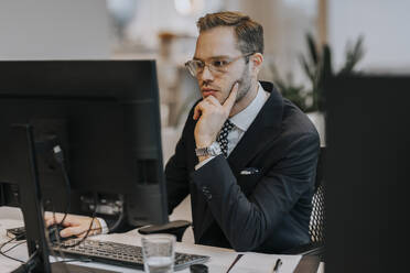 Confident young businessman using computer at desk in office - MASF42295