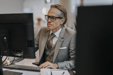 Älterer Geschäftsmann mit Brille, der einen Computer am Schreibtisch im Büro benutzt - MASF42297