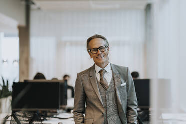 Porträt eines lächelnden reifen Geschäftsmannes mit Brille, der in einem Büro steht - MASF42301