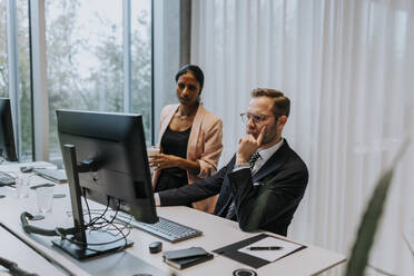 Confident businessman using computer by businesswoman standing at office - MASF42311