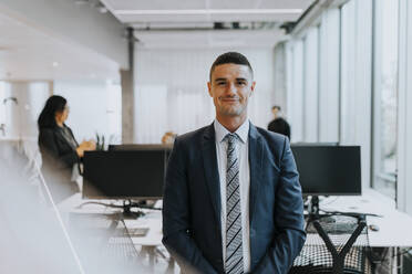 Portrait of smiling young businessman standing at corporate office - MASF42329