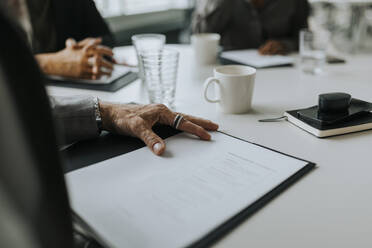 Cropped hand of mature businessman with document at conference table in board room - MASF42335