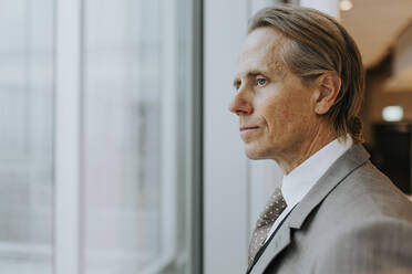 Thoughtful mature businessman looking out through window at office - MASF42388