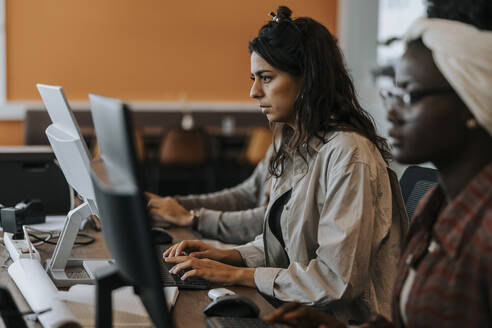 Junge Geschäftsfrau, die einen Computer benutzt und neben einer Kollegin am Schreibtisch im Büro sitzt - MASF42407