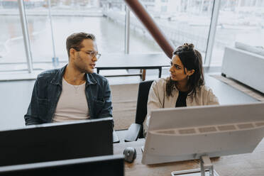 Young male and female business colleagues discussing while sitting at computer desk in office - MASF42412