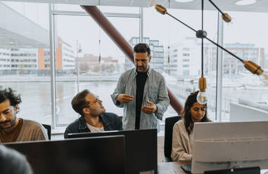 Geschäftsleute, die inmitten von Kollegen bei der Arbeit im Büro eine Strategie diskutieren - MASF42422