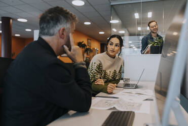 Geschäftsfrau im Gespräch mit reifem Geschäftsmann am Schreibtisch sitzend im Büro - MASF42435