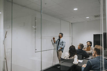 Ein reifer Geschäftsmann erklärt seinen Kollegen im Sitzungssaal die Strategie auf einem Whiteboard - MASF42448