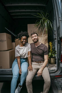 Porträt eines glücklichen Freundes und einer Freundin, die zusammen im Kofferraum eines Lieferwagens mit Kisten sitzen - MASF42464