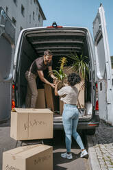 Ein gemischtrassiges Paar hilft sich gegenseitig beim Entladen von Pflanzen aus dem Kofferraum eines Lieferwagens - MASF42467