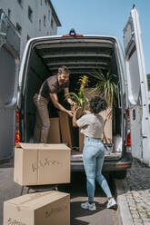 Multiracial couple helping each other while unloading plants from van trunk - MASF42467