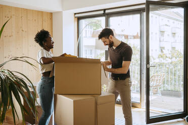 Glückliches gemischtrassiges Paar packt Kisten aus, während es in seinem neuen Haus steht - MASF42487