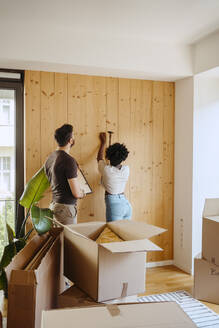 Frau hämmert Nagel in Holzwand, während sie mit ihrem Freund im neuen Haus steht - MASF42490