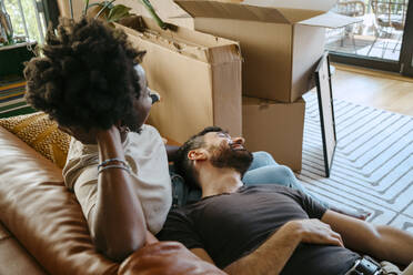 Ein gemischtrassiges Paar entspannt sich gemeinsam auf dem Sofa im Wohnzimmer seines neuen Zuhauses - MASF42496