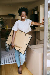 Portrait of happy woman holding frame while leaning on wall at new home - MASF42501