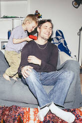 Junge hält Spielzeugpistole beim Spielen mit dem Vater, der zu Hause auf der Couch sitzt - MASF42514