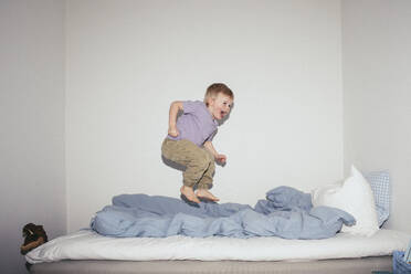 Unbekümmerter Junge, der zu Hause auf dem Bett gegen die Wand springt - MASF42516