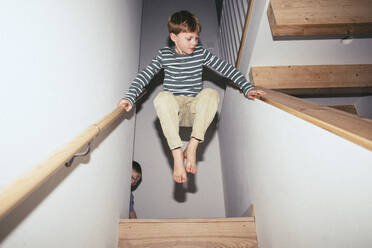 Niedriger Blickwinkel eines Jungen, der beim Spielen zu Hause in der Luft zwischen Treppen balanciert - MASF42526