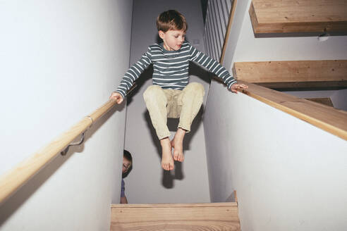 Niedriger Blickwinkel eines Jungen, der beim Spielen zu Hause in der Luft zwischen Treppen balanciert - MASF42526